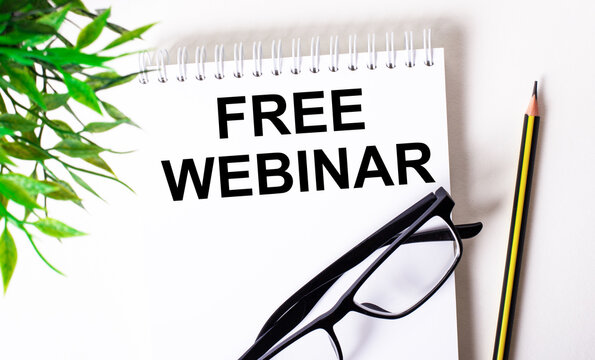 FREE WEBINAR is written in a white notebook next to a pencil, black-framed glasses and a green plant.
