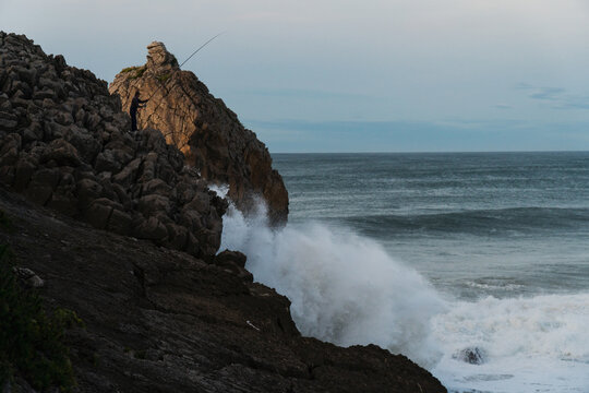 Fisher man working on a huge wavy cliff in north Spain