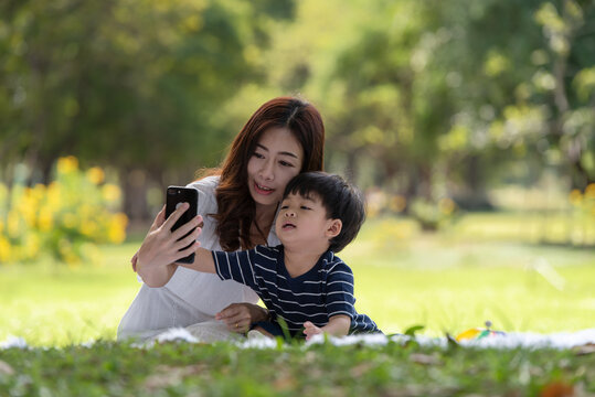 Asian family having fun mother and her son taking selfie with mobile phone in the park together, love and happiness people concept