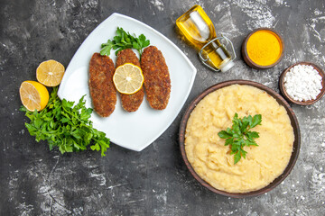 top view mashed potatoes cutlets on white plate parsley lemon slices oil on dark background