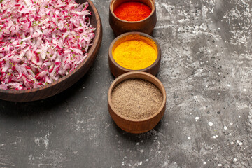 Front close view of vegetable salad with various ingredients in a brown bowl and different spices lined up in a row on dark background