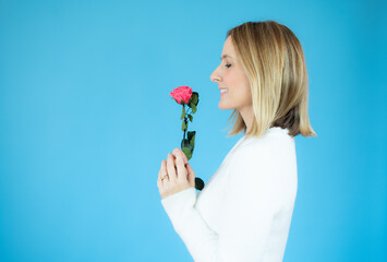 Profile portrait of young woman holding a flower over blue background.
