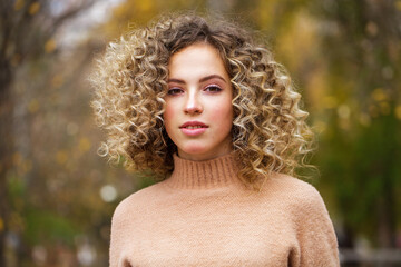 Hairstyle curly hair, portrait of a young blonde girl in an autumn park