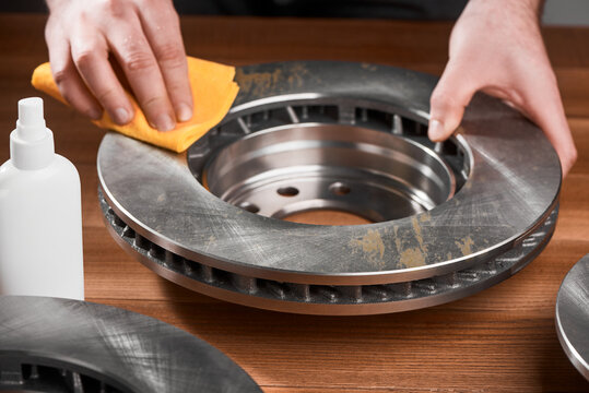 Man cleaning a brake rotor from rust, using a fabric cloth and anti rust spray