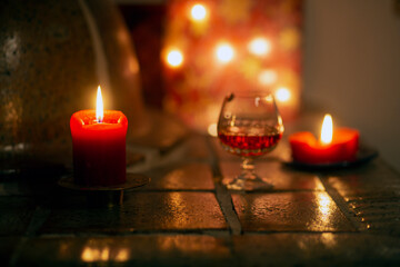 A red candle at Christmas time beside a glass of Irish whiskey on a ceramic stove.