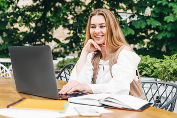 Beautiful woman working at the computer at home on the terrace. Young beautiful blonde is smiling at the computer monitor