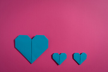 Origami hearts made with colored paper for congratulations on Valentine's Day for couples in love, on pink background
