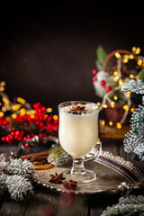 Traditional winter eggnog in a glass mug with milk, rum and cinnamon, christmas decorations