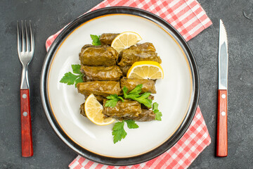top close view stuffed grape leaves on white plate knife and fork and napkin on dark background