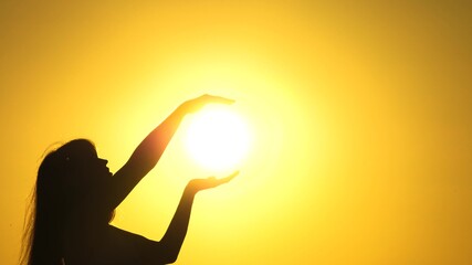 Happy woman holds sun with her hands. Silhouette of a girl praying in rays of sunset. Travel and adventure concept. Admire glory of sun. Religion and belief in God. Sunlight in girl's hands.