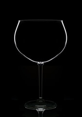 An empty wine glass in silhouette with reflection, isolated on black.