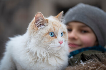 white fluffy cat with blue eyes on the shoulders of a girl in winter clothes. Concept of children and pets.