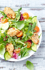 Salad with Chicken Breast, Cherry Tomatoes, Cucumber, Rocket and fresh Basil. Bright wooden background. Top view. Close up.