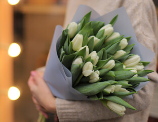 Young woman florist holding big beautiful blossoming mono bouquet of white tulip flowers.