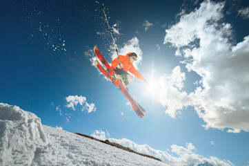 A young man skier in sunglasses and shorts makes a jump trick on a background of blue sky and...