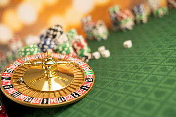  Casino concept.  Roulette wheel, poker chips and dice on green table and on  yellow bokeh background.  © zolnierek