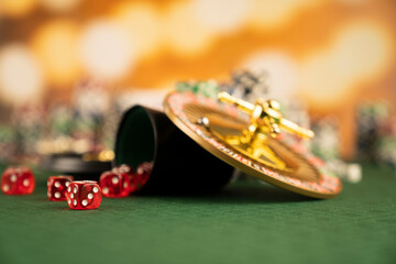 
Casino concept.  Roulette wheel, poker chips and dice on green table and on  yellow bokeh background.
