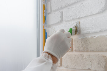 Worker is painting a brick wall with a brush.