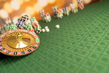 
Casino concept.  Roulette wheel, poker chips and dice on green table and on  yellow bokeh background.
