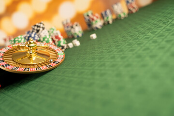 
Casino concept.  Roulette wheel, poker chips and dice on green table and on  yellow bokeh background.
