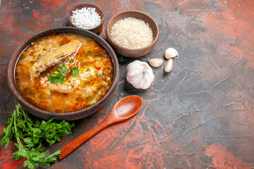 bottom view homemade chicken and rice soup in a bowl wooden spoon bowls with sea salt and rice garlic on dark red background with copy space