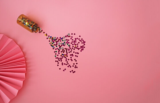 Heart-shaped confetti scattered from a bottle on a pink background 