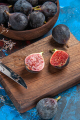 Above view of fresh black mission figs in a small brown pot on wooden cutting board and knife on blue background