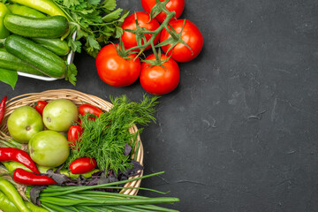 Above view of two vegetable baskets with a bunch of green and peppers cucumber and tomatoes with stem on dark background
