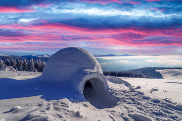 Real snow igloo house in the winter mountains glowing by morning sunlight. Incredible purple sunset...