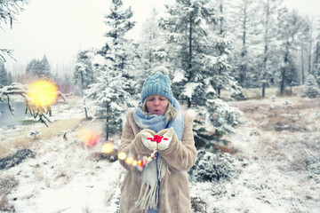 Fototapeta na wymiar Frau pustet rote Herzen aus der Hand im Wald im Winter