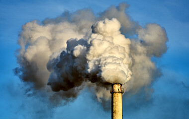 White steam cloud and smoke clouds rise from a high chimney into the blue sky