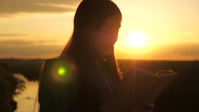 A girl holds Bible in his hands and studies word of God at sunrise on top of mountain. A woman reads a book in rays of the sun. Man reads Bible outdoors. Searching for truth in scriptures.