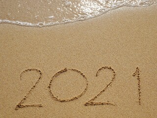 Handwriting year 2021 on beautiful sand and foam wave on beach.