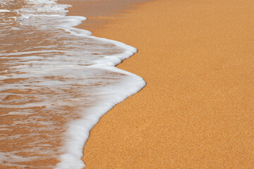 Close up view of white foam on a yellow sandy seashore with selective focus