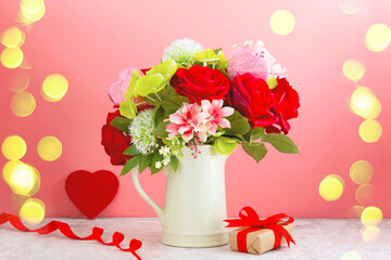 Colorful flower bouquet arrangement with red roses in vase on pink background with bokeh lights.