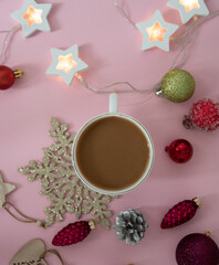 Obraz na płótnie Canvas A composition of Christmas decorations, Christmas balls, toys, garlands and a Cup of coffee for a pleasant pastime on a pink background.