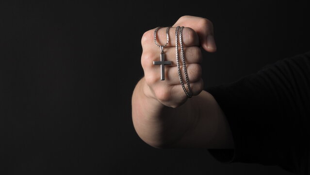 Cross or crucifix pendant and necklace in man hand on black color background in studio which represent praying for god or jesus and thank gods for giving peaceful and faithful to people. silver cross.