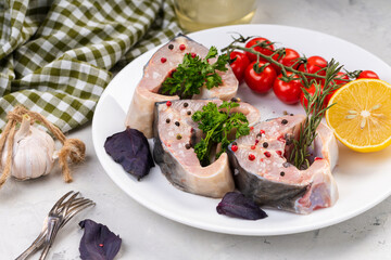 Fresh organic seafood. Raw sturgeon steaks on a white plate with spices and vegetables. On a gray background. Side view