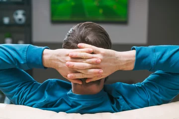 Fotobehang Back view close up of a man relaxing at home sitting on sofa and watching football play on tv © wpadington