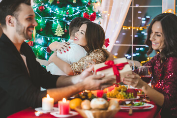 Beautiful happy young friends celebrating Christmas or New year together sitting at the holiday decorated table having fun and sharing gifts