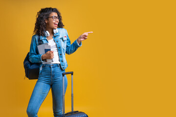 Smiling dark skinned female tourist isolated over bright colored yellow background pointing with...