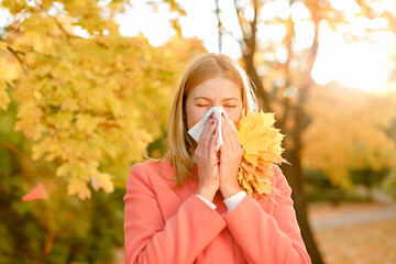 A girl with a raft sneezes in the fall. Runny nose and other cold symptoms. Allergy.