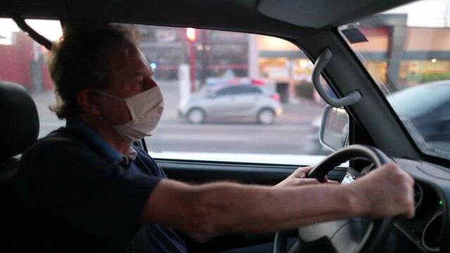 Older man driving car while wearing covid-19 face mask
