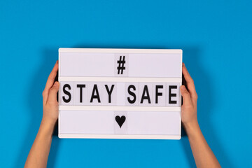 Hands holding lightbox with message Stay Safe on light blue background. isolated. Healthcare, social distancing concept. Top view