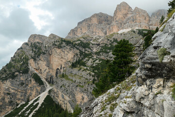 Fototapeta na wymiar A view on a sharp and stony mountain wall in Italian Dolomites. The massive mountain is surrounded by clouds. Lower parts overgrown with trees. Remote and desolate landscape. Silence before the storm