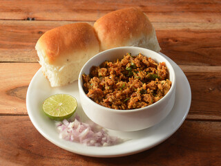 Paneer bhurji with Pav is a spicy paneer curry dish made up of paneer, onion, tomatoes and indian spices served with buns or pav, isolated over a rustic wooden background, selective focus