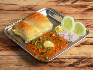 Pav Bhaji is a fast food dish from India, Thick and spicy vegetable curry, served with a soft bread roll or Bun Paav and butter. isolated over a rustic wooden background, selective focus