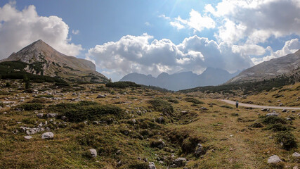 Fototapeta na wymiar A gravelled pathway leading through Italian Dolomites. High, sharp mountains around. The slopes and meadow are golden, higher parts barren and stony. Remote and desolate place. Freedom and calmness