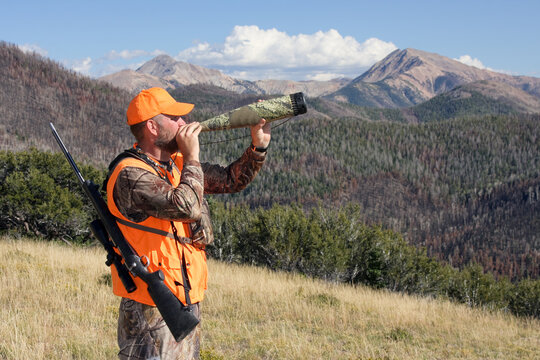 Adult Rifle Hunter Blowing Elk Calls Through Bugle Tube In Mountains