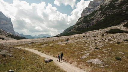 Obraz premium A couple hiking along a gravelled pathway leading through a valley in Italian Dolomites. High, sharp mountains around. Stony and raw landscape. Remote and desolate place. Freedom of exploration